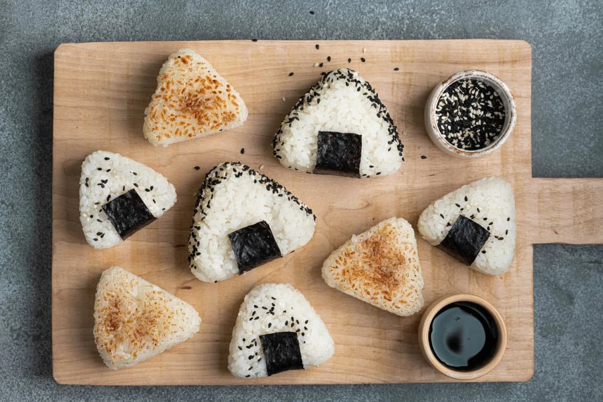 Trójkątne onigiri z nori i sezamem oraz opiekane onigiri na drewnianej desce, widok z góry